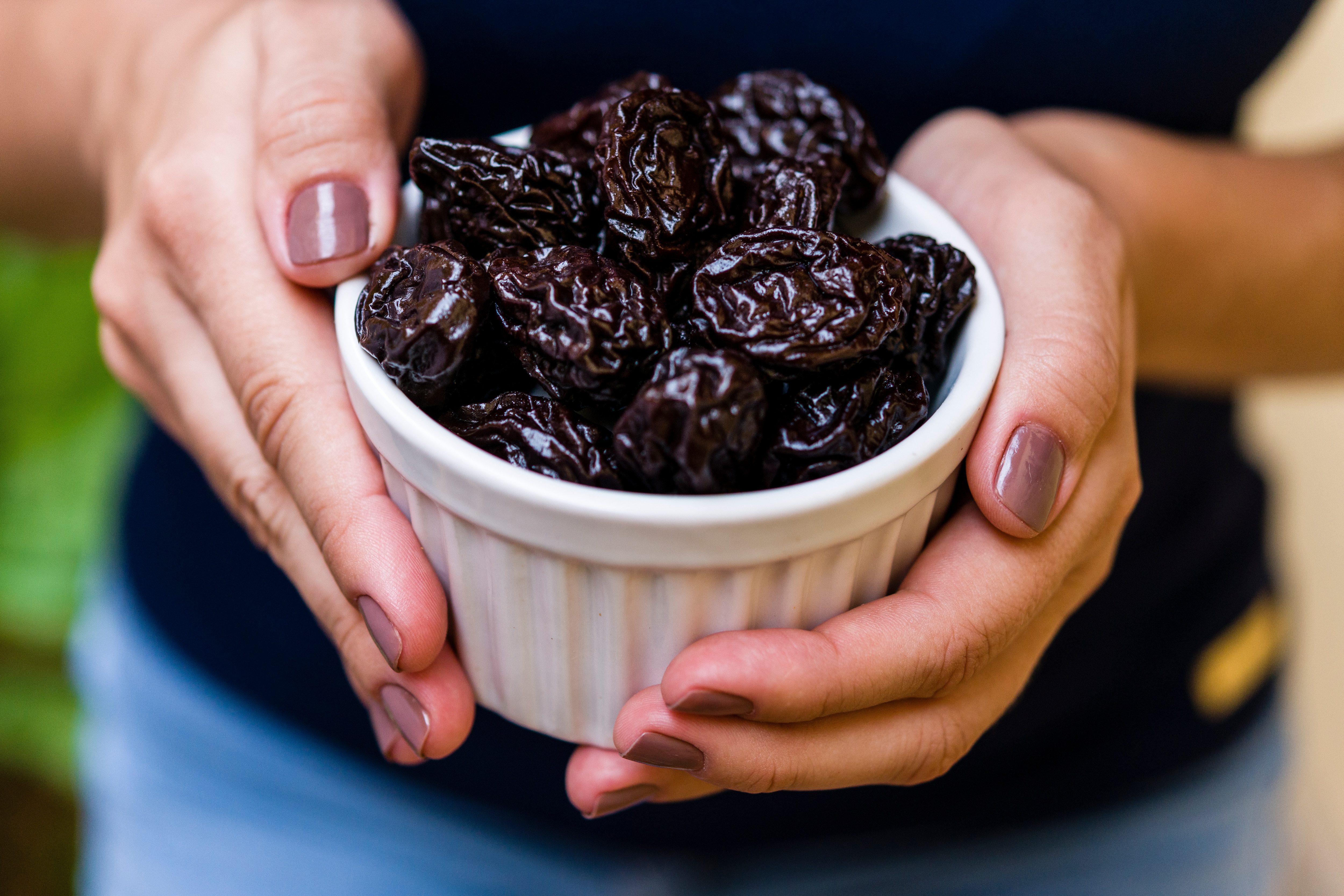 Woman holding a white, ceramic ramekin filled with delicious, dried plums or prunes (thumbnail  image).