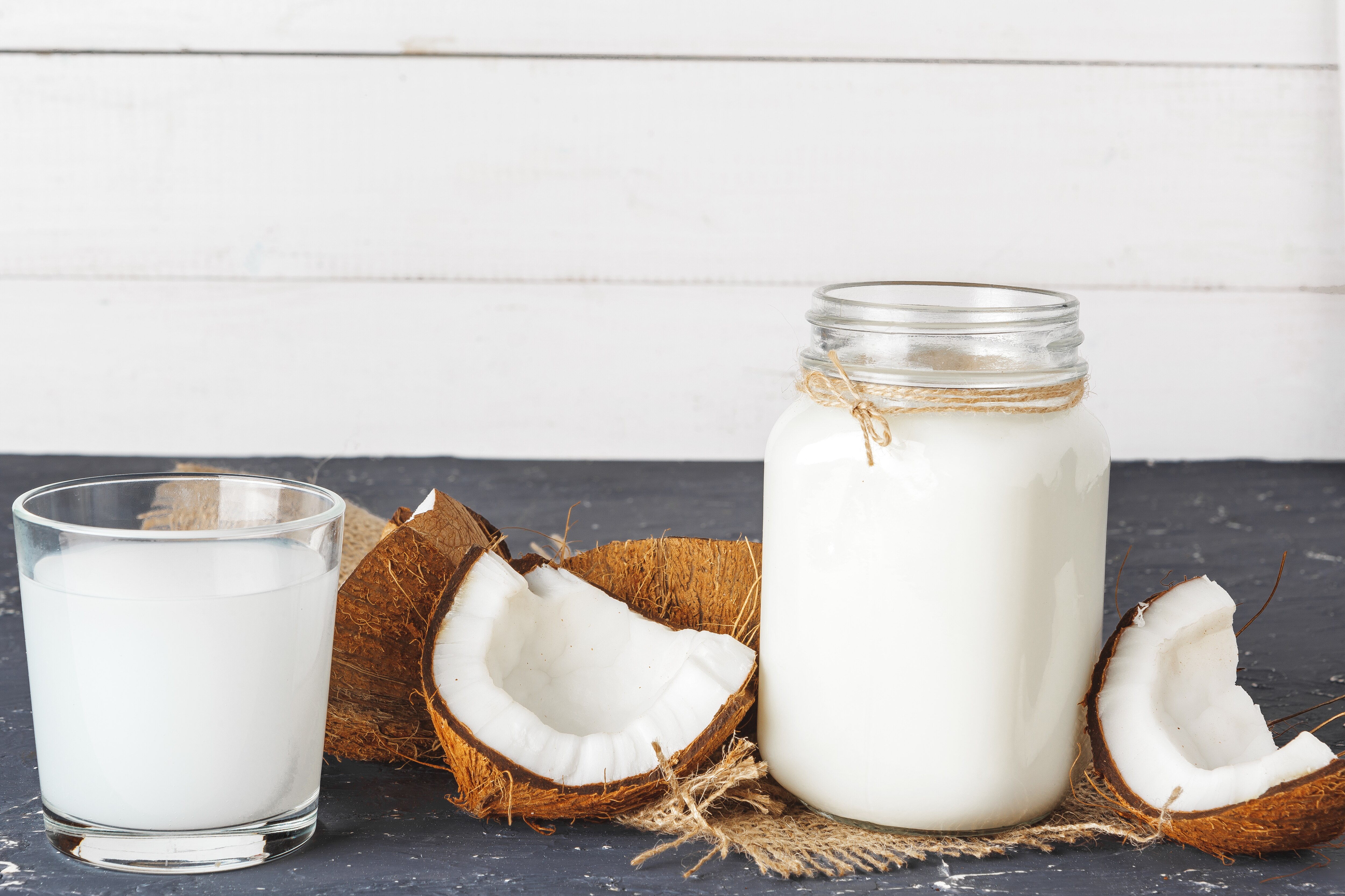 Creamy homemade coconut yogurt in a glass jar with fresh coconut milk on a granite table. Dairy-free probiotic-rich plant-based yogurt for gut health and digestion.
