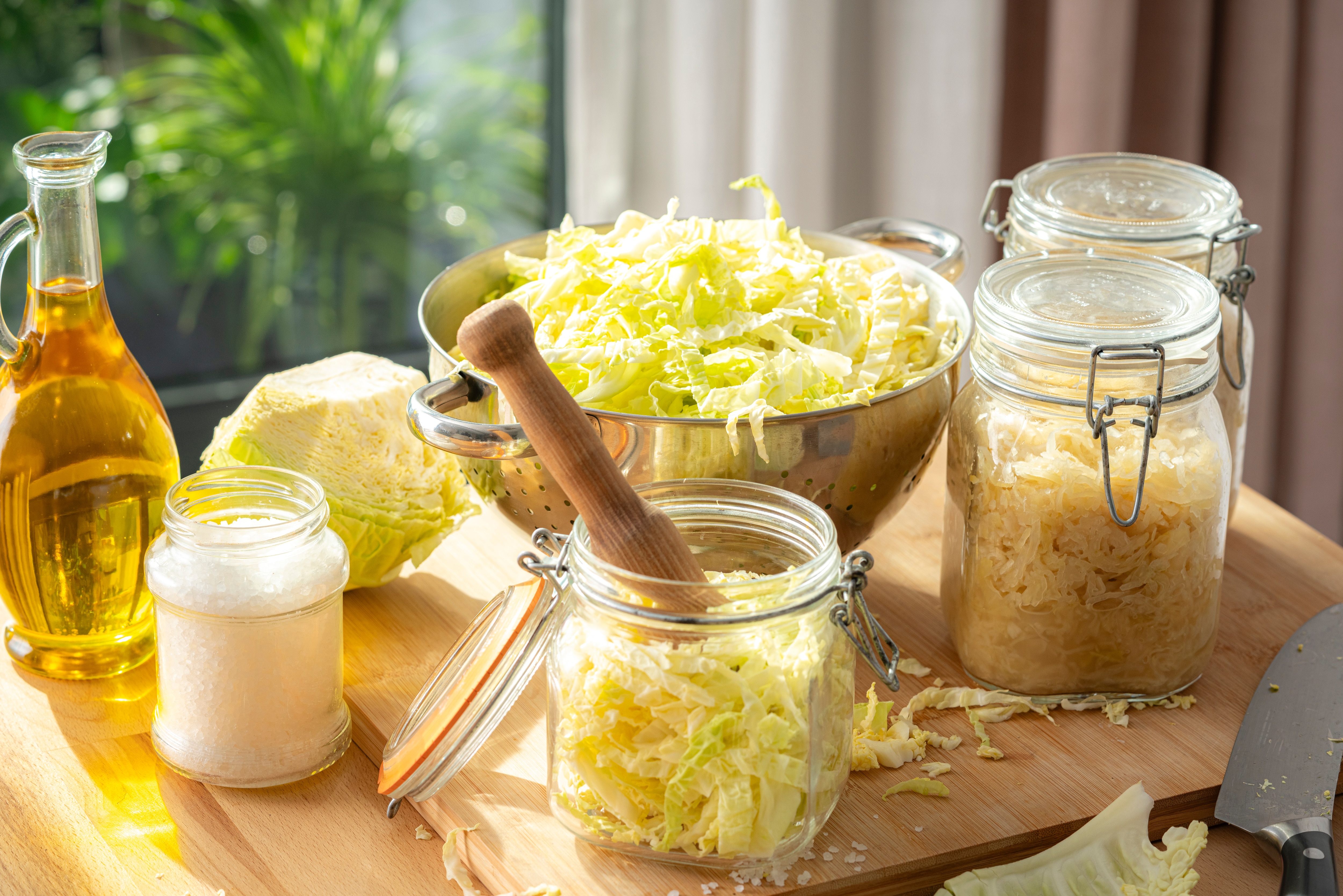 Homemade fermented sauerkraut in a glass jar with fresh cabbage and sea salt on a rustic kitchen table. Probiotic-rich fermented food for gut health and digestion.
